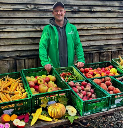 KI generiert: Das Bild zeigt den Kopf einer neugierig wirkenden Ziege, die zwischen Holzlatten hervorschaut. Auf dem Bild ist der Text "Hallo Du!" zu sehen.