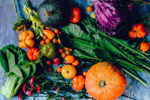 KI generiert: Verschiedene bunte Gemüse und Blätter, wie Kürbisse, Paprika und Kohl, auf blauem Hintergrund.