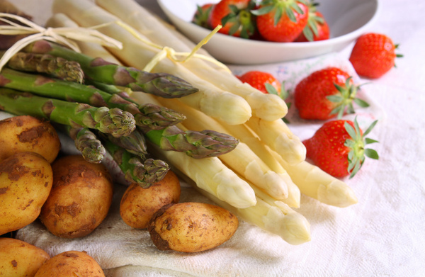 KI generiert: Weißer und grüner Spargel, Kartoffeln und Erdbeeren auf einem Tisch arrangiert. Kein Text vorhanden.