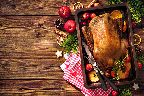 KI generiert: Gebratene Gans in einer Backform, umgeben von Äpfeln, Gewürzen und Tannenzweigen auf einem Holztisch.