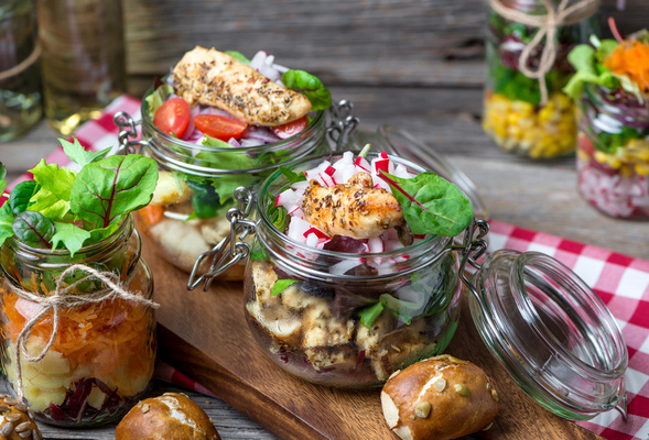 KI generiert: Verschiedene bunte Salate in Einmachgläsern, dekoriert mit Gemüse und Hähnchen auf einem Holztisch.