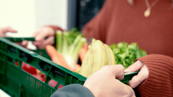 KI generiert: Eine grüne Kiste voller frischem Gemüse und Obst wird übergeben.