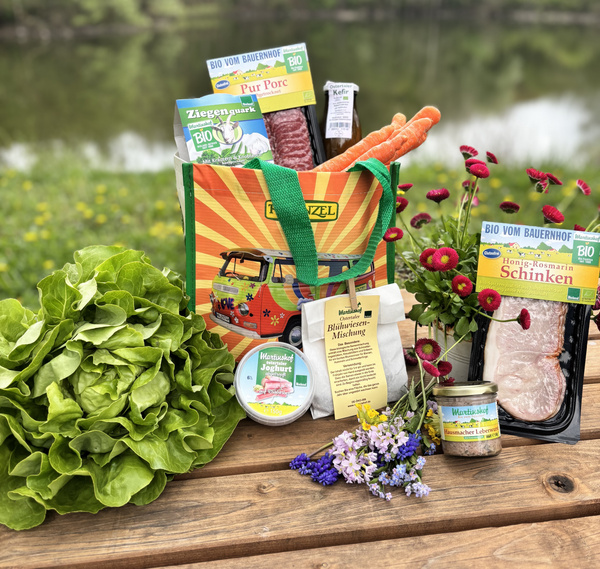 KI generiert: Bioprodukte in einer Tasche, umgeben von Gemüse, Blumen und einem Salatkopf, auf einem Holztisch im Freien.