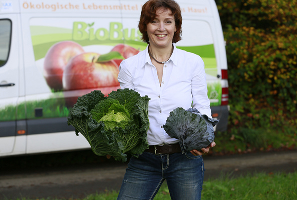 KI generiert: Eine Frau hält Kohlköpfe, vor einem Lieferwagen mit der Aufschrift "BioBus - Ökologische Lebensmittel".