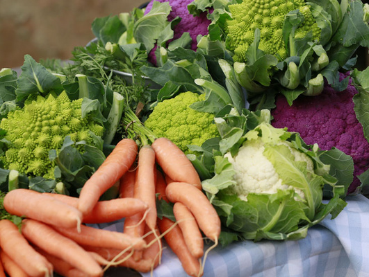 KI generiert: Frisches Gemüse: Karotten, grüner und lila Blumenkohl auf einem karierten Tuch arrangiert.