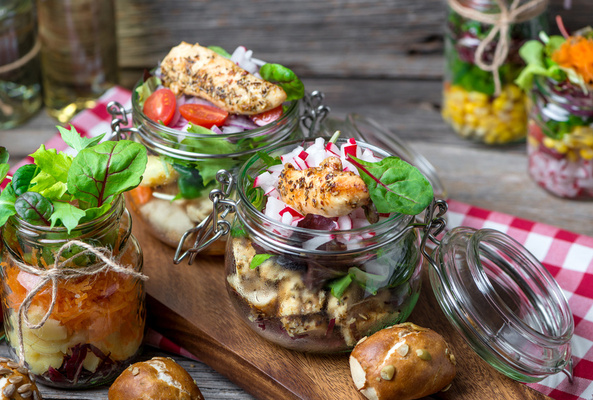 KI generiert: Salate in Einmachgläsern mit frischem Gemüse und Hähnchen auf einem Holzbrett serviert.