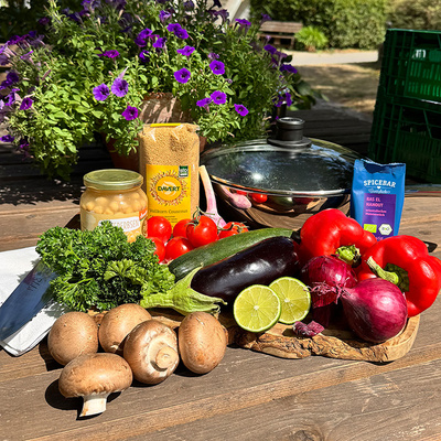 KI generiert: Frisches Gemüse, eine Packung Couscous und Gewürze auf einem Tisch arrangiert, umgeben von Blumen.