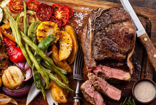 KI generiert: Gegrilltes Fleisch mit geschnittenem Steak und bunter Vielfalt an Gemüse auf einem Holzbrett.